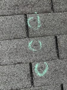 Hail damage marked with chalk circles on shingles during roof inspection in St. Louis