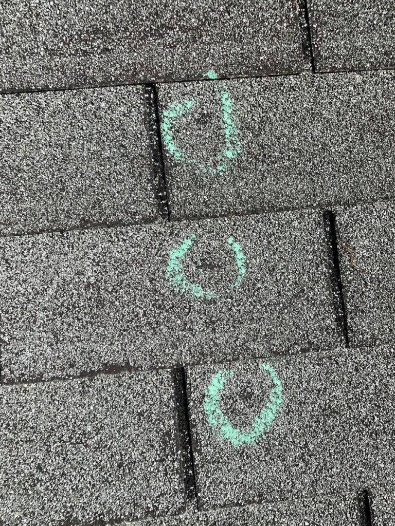 Hail damage marked with chalk circles on shingles during roof inspection in St. Louis