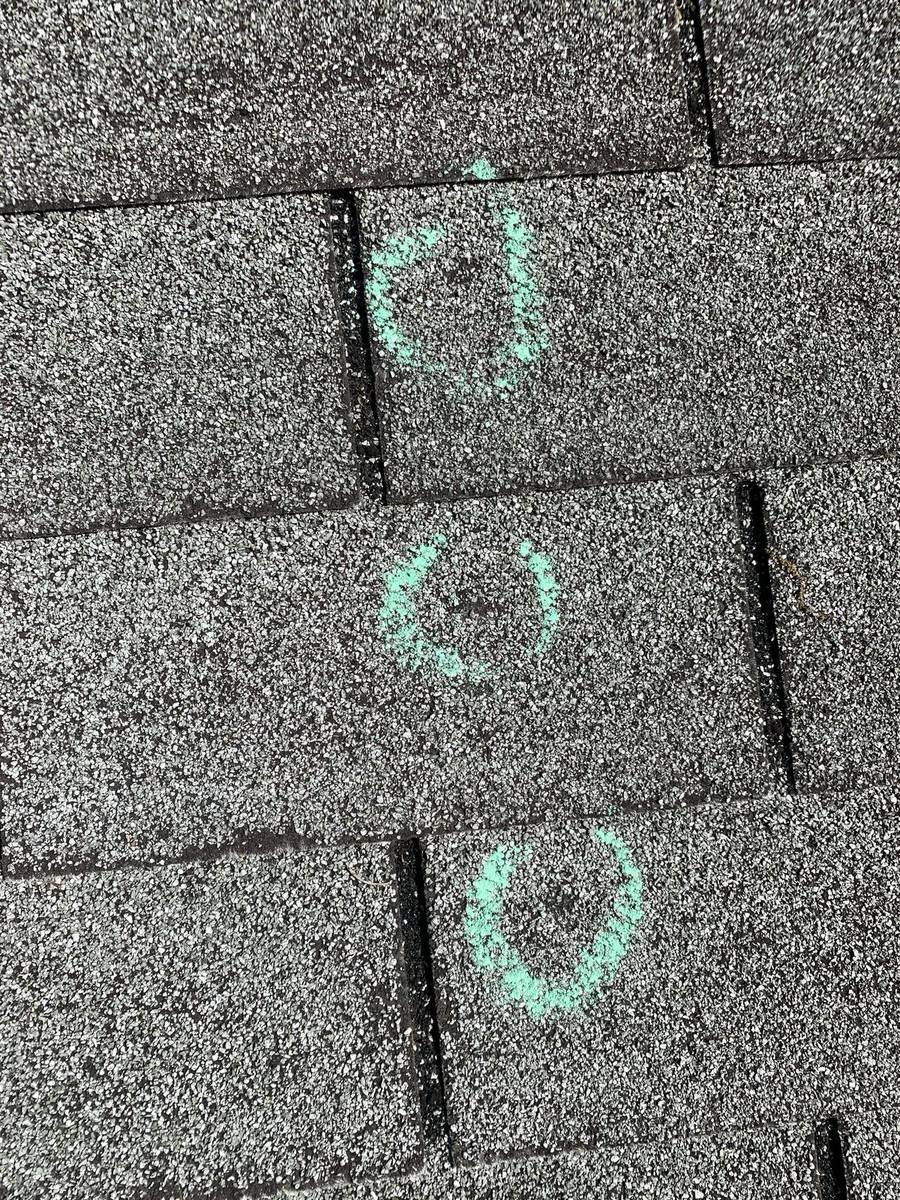 Hail damage marked with chalk circles on shingles during roof inspection in St. Louis