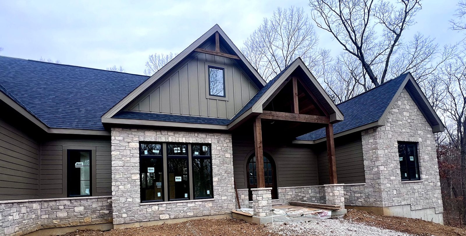 Dark olive James Hardie lap siding with stone columns and timber frame entry in St. Louis MO